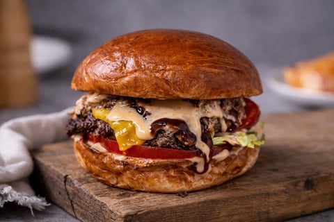 Gourmet burger with melted cheese, caramelized onions, and roasted red peppers on a toasted brioche bun, served on a wooden board