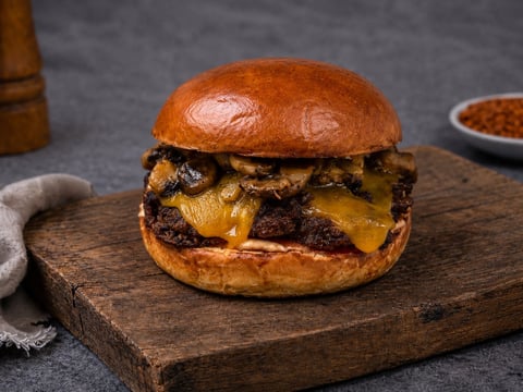 Gourmet cheeseburger with caramelized onions and melted cheese on a toasted bun, served on a wooden board
