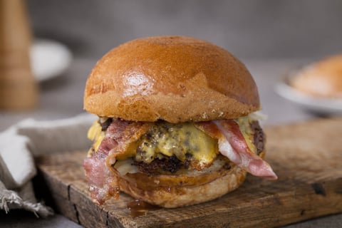 Gourmet burger with melted cheese and crispy bacon on a toasted bun, served on a wooden board