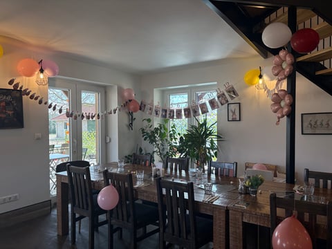 Modern dining room decorated with pink and gold balloons, plants, and string lights for a celebration or party