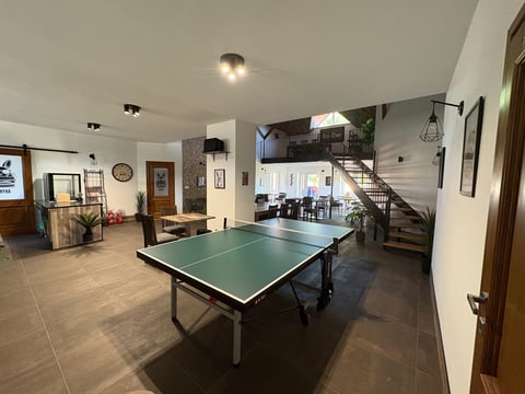 Spacious indoor recreation room with a green ping pong table in the center, stairs, kitchen area, and various furniture and decorations.
