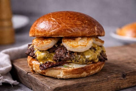 Gourmet burger with beef patty, melted cheese, grilled onions on toasted bun, served on wooden board