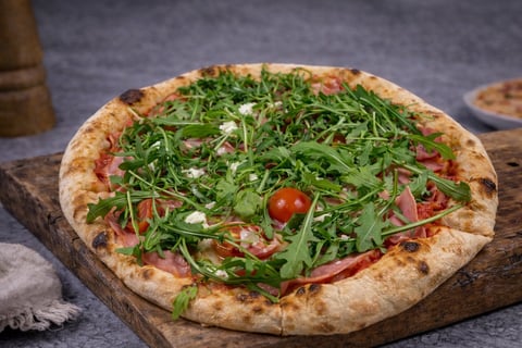 Gourmet pizza with arugula, tomatoes, and white cheese on wooden board