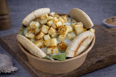 Cardboard bowl with two white bread rolls and golden fried tofu cubes on a wooden board