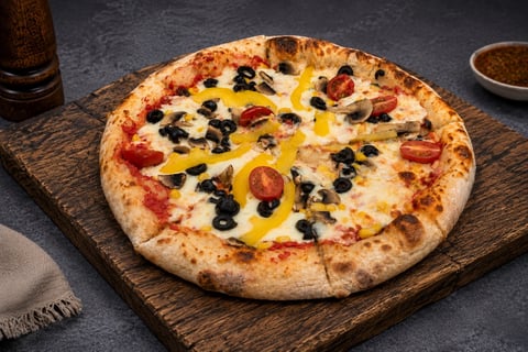 Freshly baked pizza topped with red peppers, black olives, and yellow peppers on a wooden serving board