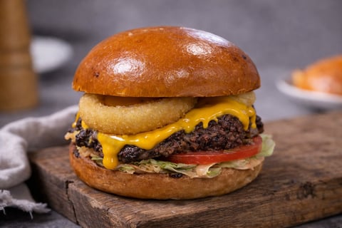 Gourmet hamburger with melted cheese, beef patty, and fresh lettuce and tomato on a sesame bun, served on a wooden board