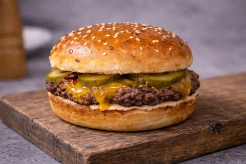 Cheeseburger with pickles and melted cheese on a sesame seed bun, served on a wooden board