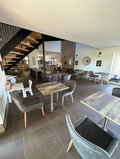Modern open-concept interior with dining tables, black staircase, and contemporary furnishings in neutral tones