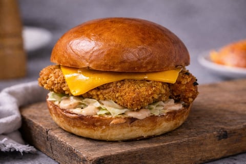 Crispy fried chicken sandwich with melted cheddar cheese and coleslaw on a toasted bun, served on a wooden board