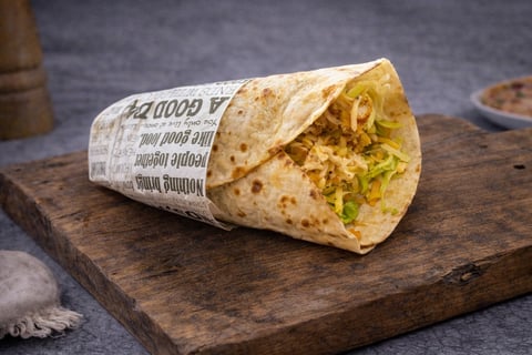 Wrapped burrito filled with yellow rice and vegetables on a wooden cutting board