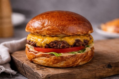 A gourmet cheeseburger with melted cheese, beef patty, tomato, and lettuce on a toasted brioche bun, served on a wooden board