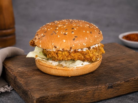 Crispy fried chicken sandwich with coleslaw on a seeded bun, served on a wooden board