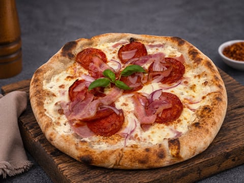 Pepperoni pizza with fresh basil on a wooden board, served with beer and condiments on a dark background