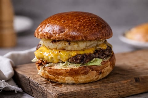 Gourmet burger with golden brioche bun, melted cheese, beef patty, and fresh lettuce on a wooden board