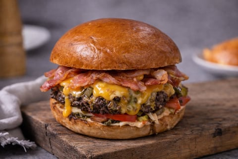 Gourmet burger on wooden board with crispy bacon, melted cheese, and mushrooms on toasted bun